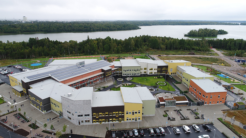 Flygfoto över Pär Lagerkvistskolan. Flera byggnader som omsluter en innergård samt en sjö och träd i bakgrunden.